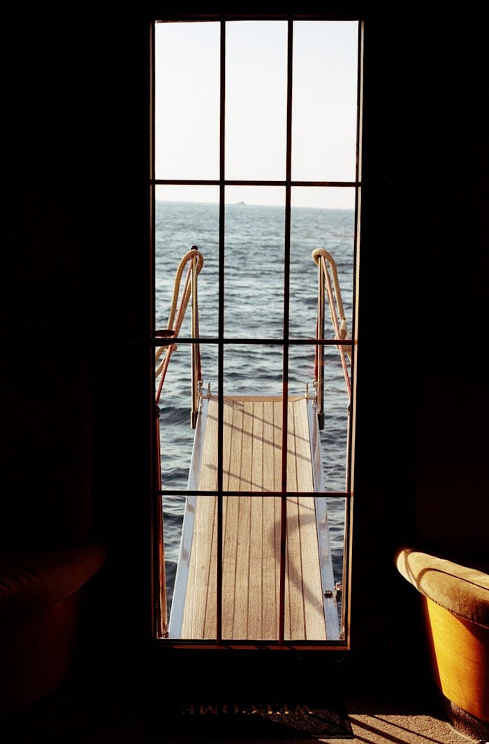 A serene view of the open sea framed by a window with a wooden gangway leading out.