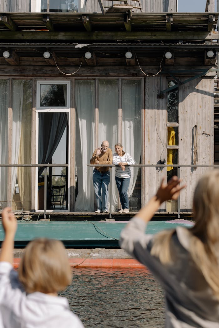 Home A heartwarming moment as an elderly couple waves from their houseboat to visiting family members on a sunny day.